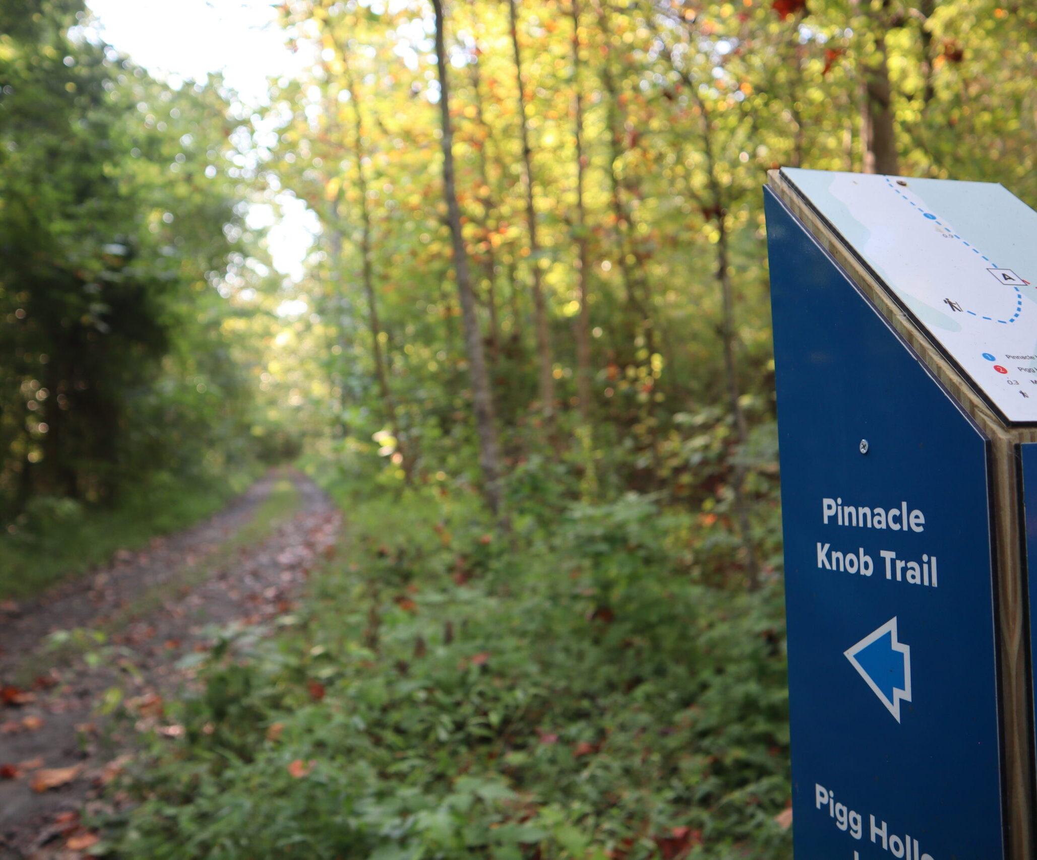 A blue signpost points the way to the new Pinnacles Knob Trail in the background.