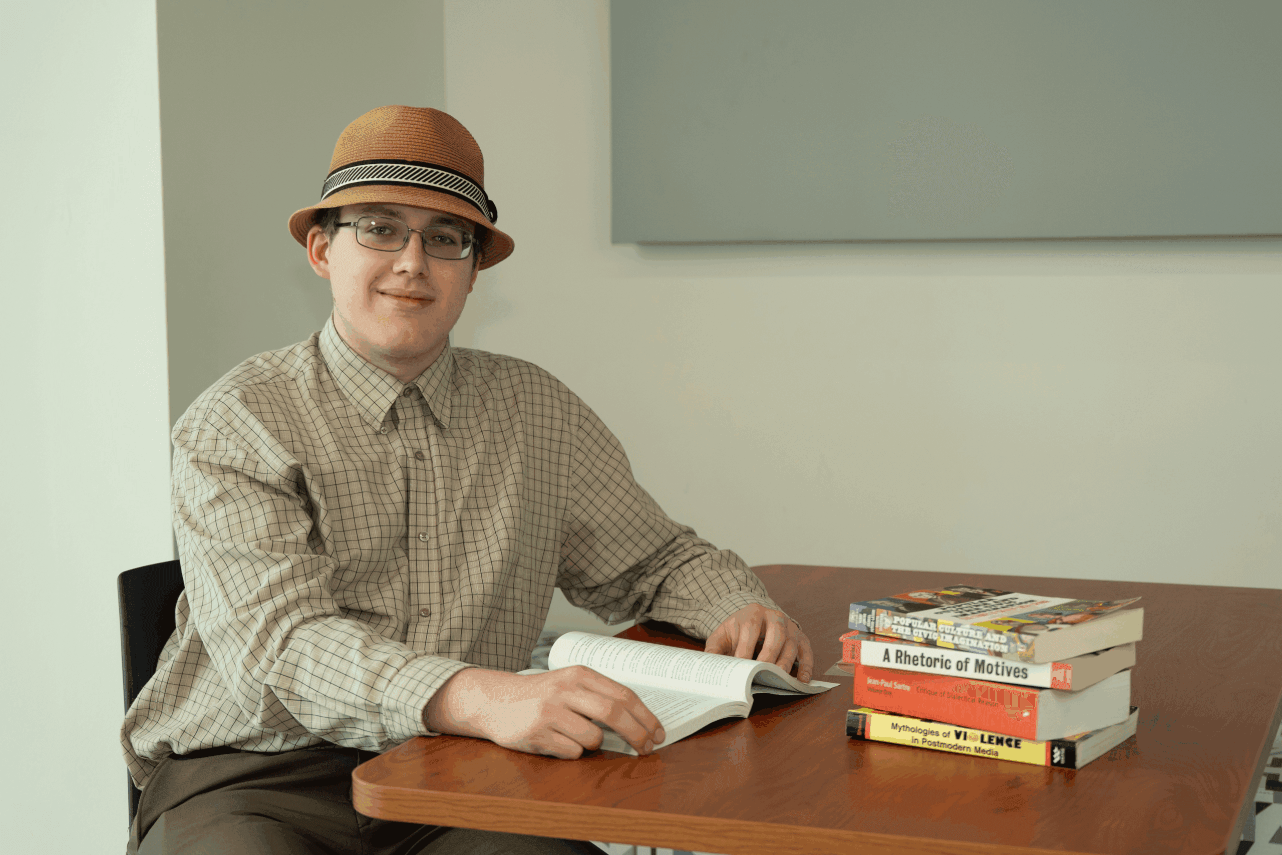 Student, Sam, smiling at the camera while sitting at a table with books.